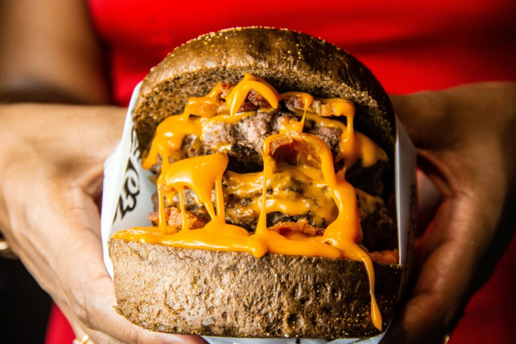 pexels-photo-3826273-3826273 Close-up of a juicy cheeseburger with bacon and melted cheese in hands, perfect for fast food lovers.