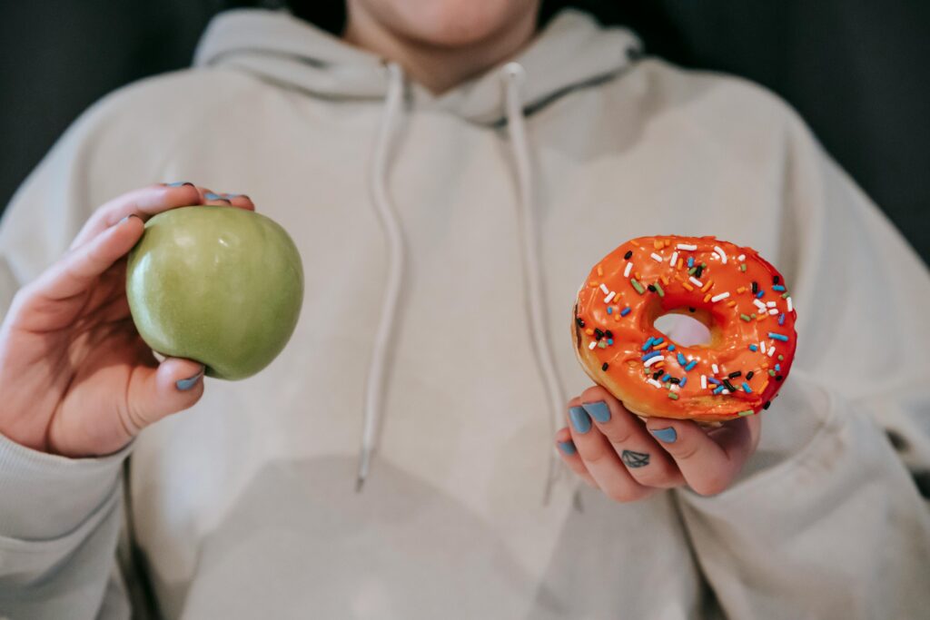 pexels-photo-6550793-6550793 A person holding both an apple and a donut, symbolizing a food choice dilemma.