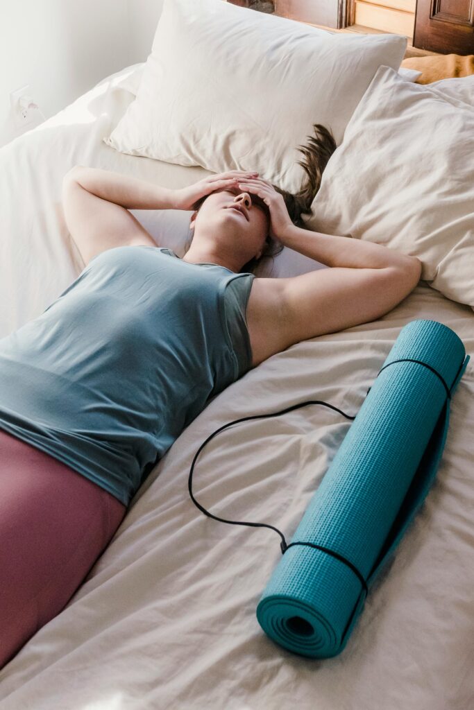pexels-photo-6697404-6697404 Adult woman in activewear resting on bed with yoga mat nearby, symbolizing post-exercise relaxation.